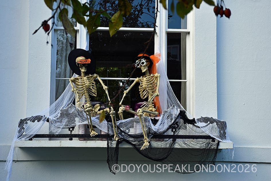 Two skeletons in hats sitting in a window decorated with cobwebs on Clifton Hill, St John's Wood